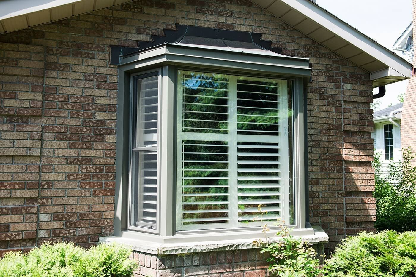 Custom Made Bay Window With Dark Grey Trim On The Side of Brick Home